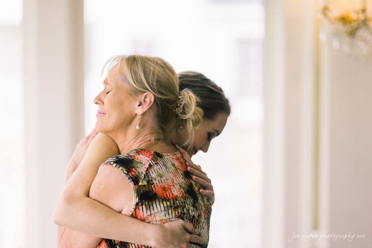 charlotte wedding photographers - ashley & matt Two women are embracing warmly in a softly lit interior. The woman on the left has her eyes closed, expressing a serene smile, while the woman on the right is partially visible, her hair styled in an updo.