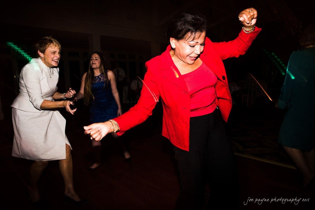 charlotte wedding photographers - ashley & matt A group of people dancing energetically at an indoor event. A woman in a red outfit stands out in the foreground, while others in dresses enjoy the moment in the background. The lighting creates a lively atmosphere.