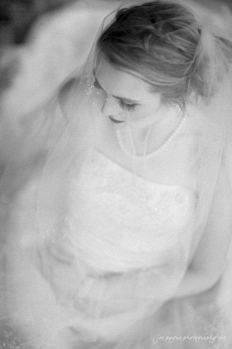 charlotte wedding photographers - ashley & matt A black-and-white photo of a bride wearing a veil and a pearl necklace, looking downward. The image has a soft focus, creating a dreamy and ethereal atmosphere.