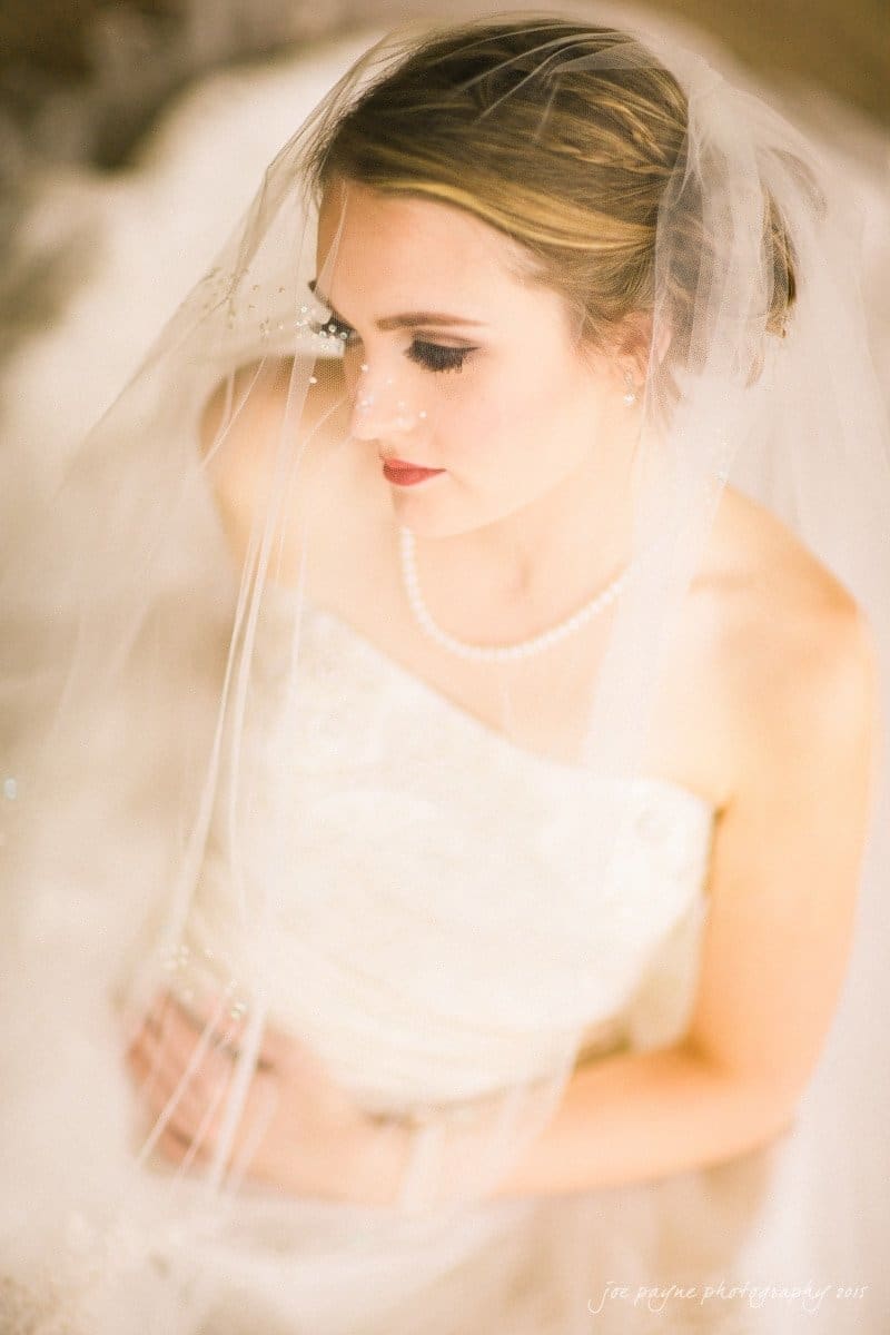 charlotte wedding photographers - ashley & matt Bride in a white wedding dress and veil, looking downwards with a soft expression. She is wearing pearl jewelry and is surrounded by a softly blurred background, giving a dreamy and ethereal feel.
