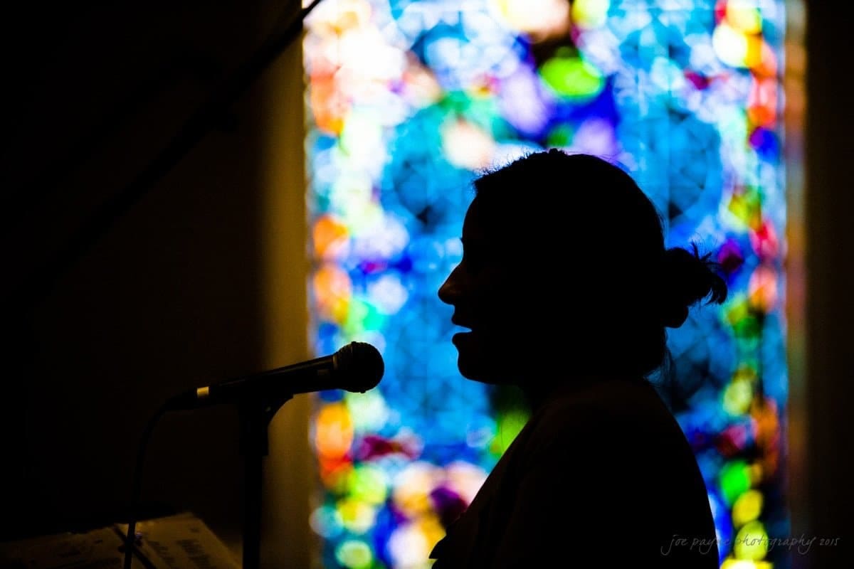 Silhouette of a person speaking into a microphone, with a vibrant, colorful stained glass window in the background.