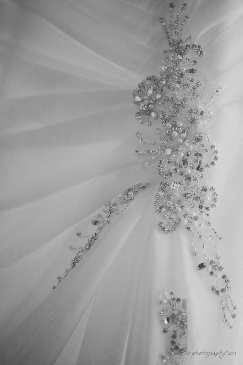 Close-up of a white wedding dress with intricate beadwork and embroidery. The design features shimmering crystals and delicate floral patterns on flowing fabric, creating an elegant and sophisticated look.