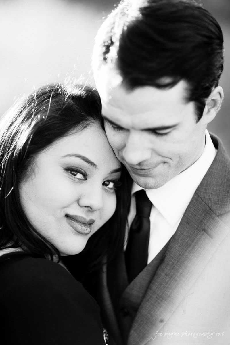 duke gardens engagement photography - yasmin & mike A black and white photo of a smiling couple embracing. The woman looks at the camera while resting her head on the mans shoulder. The man is wearing a suit and is looking down with a gentle smile.