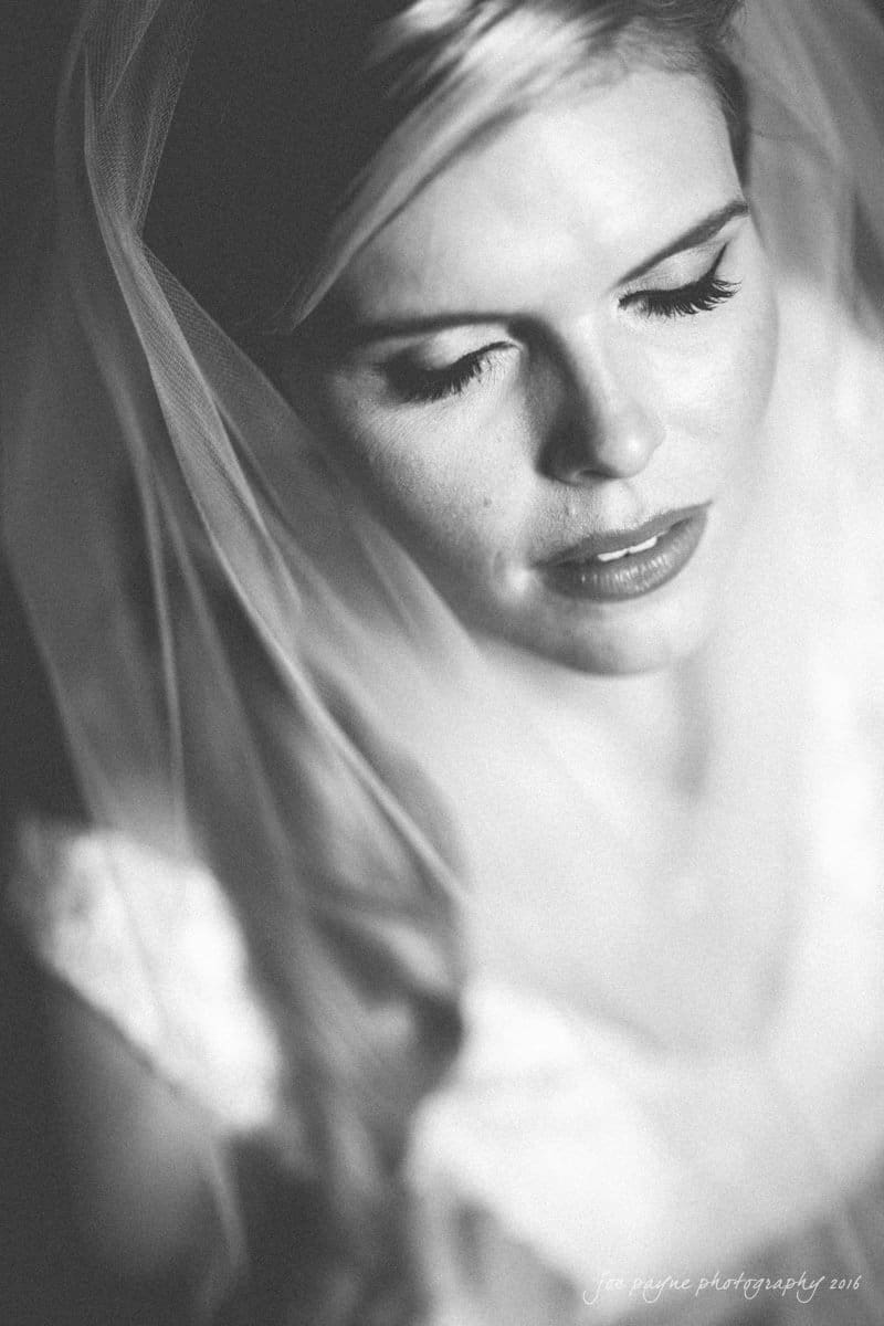raleigh bridal photography session - jackie at the sutherland Black and white photo of a bride with closed eyes, wearing a veil. The image has a soft focus, capturing an intimate and serene moment. Shadows and light play across her face, highlighting her eyelashes and lips.