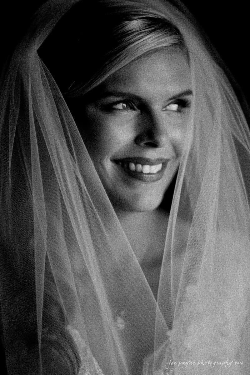 raleigh bridal photography session - jackie at the sutherland A black and white photo of a smiling bride wearing a veil, looking to the side. The image captures a serene and joyful expression.