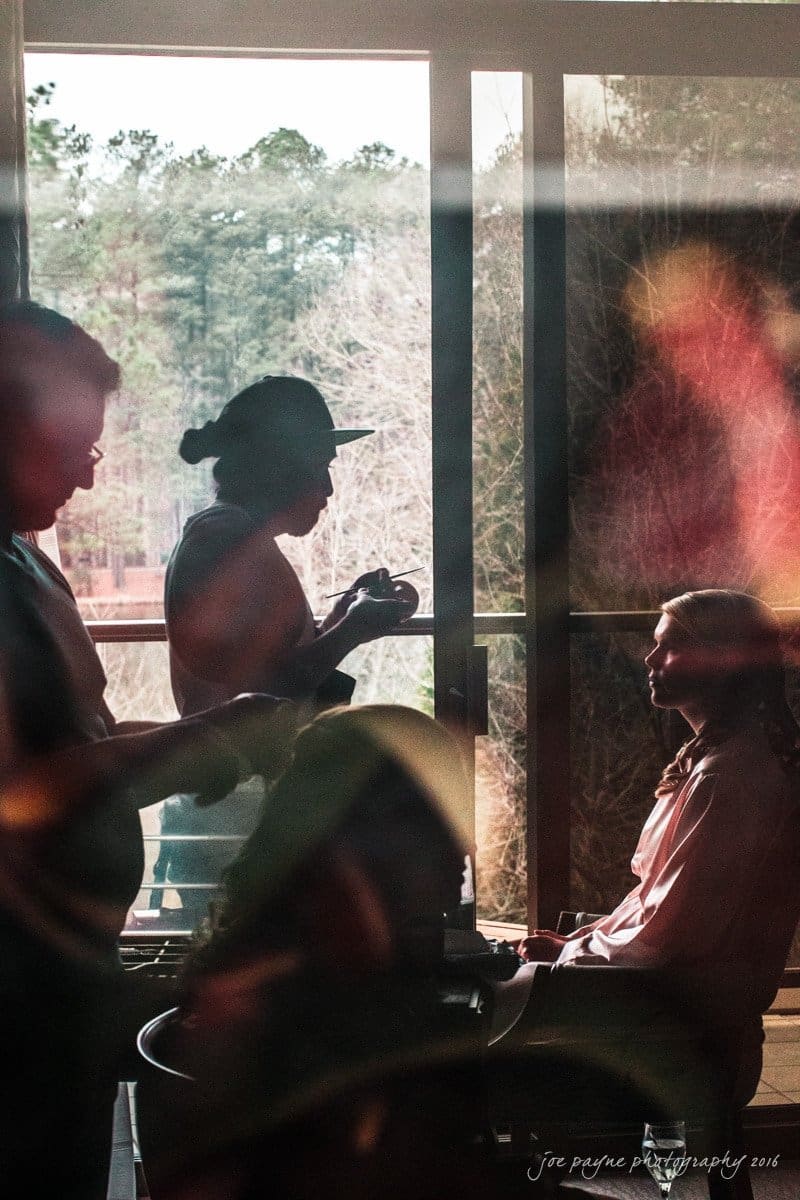 st. mary's chapel raleigh wedding photography - jackie & rob A silhouette of a photographer taking a picture of a person sitting indoors by a large window. Natural light streams in, illuminating the scene, with trees visible outside.