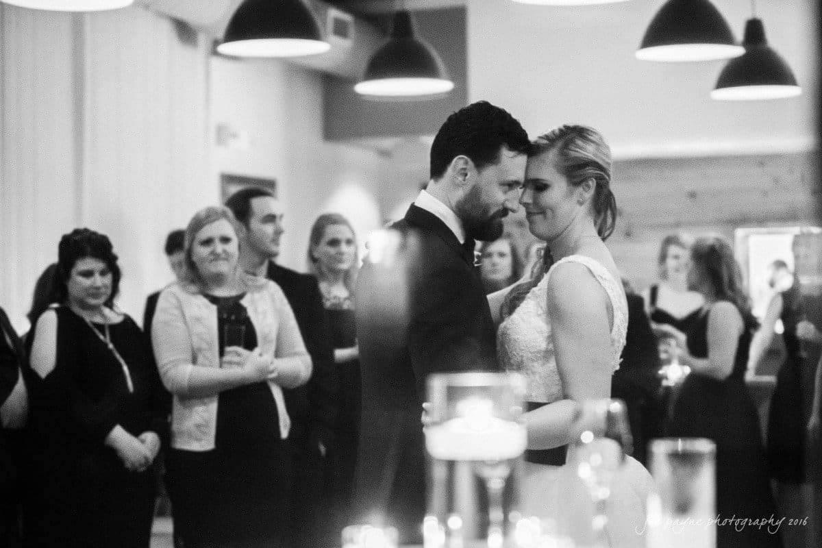 st. mary's chapel raleigh wedding photography - jackie & rob A bride and groom share a romantic first dance at their wedding reception, surrounded by guests. The room is softly lit, creating an intimate atmosphere.