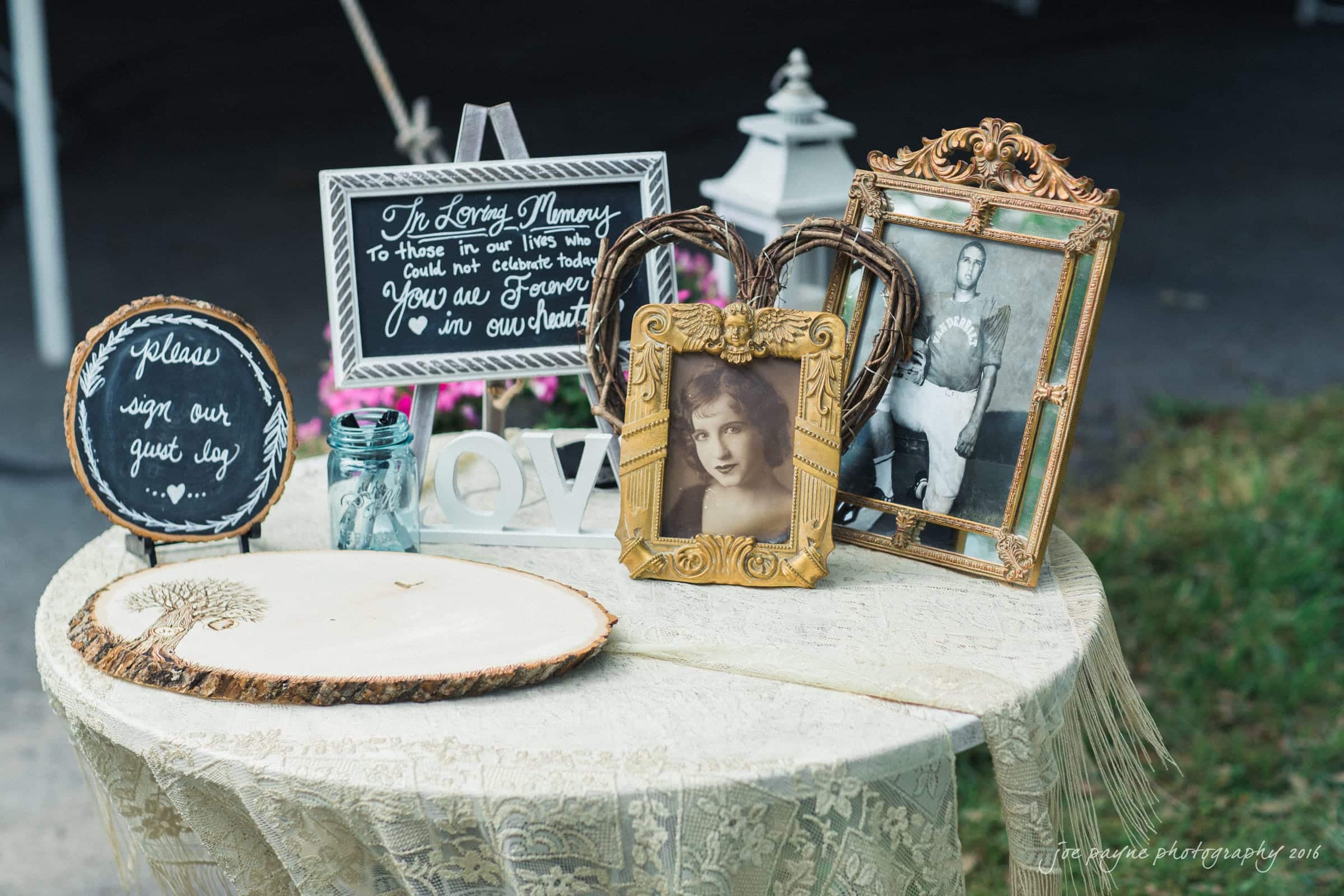 new bern wedding photographer - jessica & brinson A small round table is adorned with ornate picture frames, a wooden LOVE sign, and a chalkboard with a message honoring loved ones. A guestbook is also displayed on a rustic wood slab.