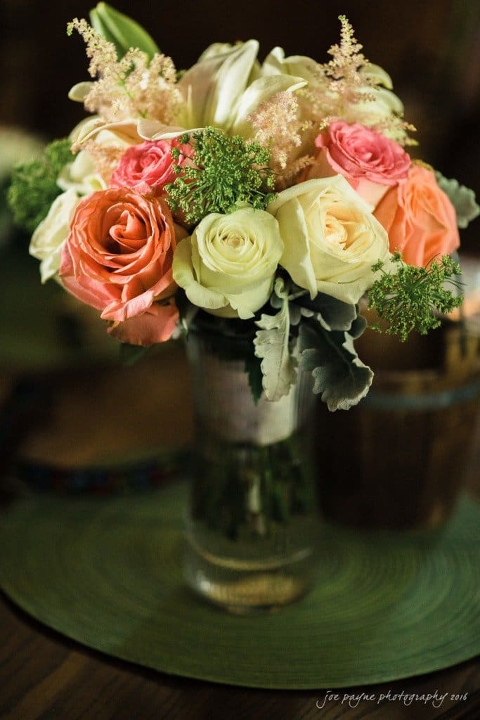 new bern wedding photographer - jessica & brinson A bouquet of pink, peach, and white roses mixed with green and white foliage, arranged in a glass vase on a green placemat.