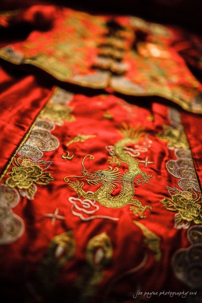 Close-up of an intricately embroidered red textile featuring a golden dragon and floral patterns. The fabric appears luxurious, with vibrant colors and detailed stitching.
