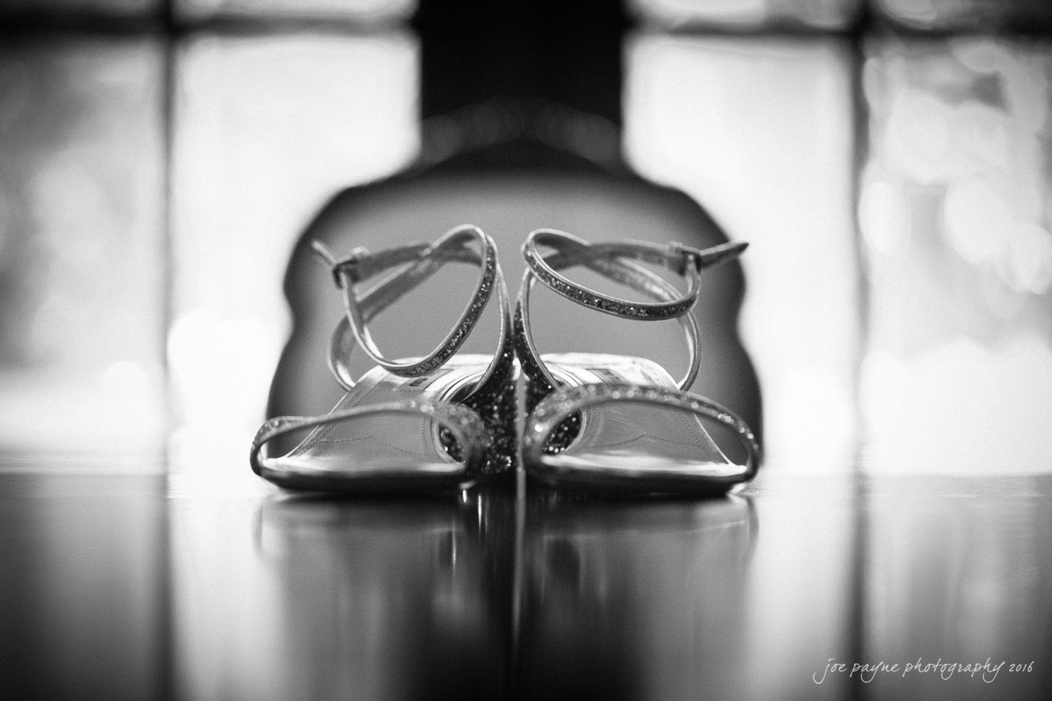 the oaks at salem wedding photography - kathryn & justin Black and white image of a pair of sparkling high-heeled sandals resting against each other on a reflective surface. The shoes are centered with a blurred background, creating a soft and elegant atmosphere.