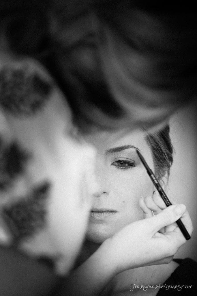 the oaks at salem wedding photography - kathryn & justin Close-up of a person having their eyebrows styled with a pencil, focusing intently. The image is in black and white, capturing a serene and detailed moment in the makeup process.