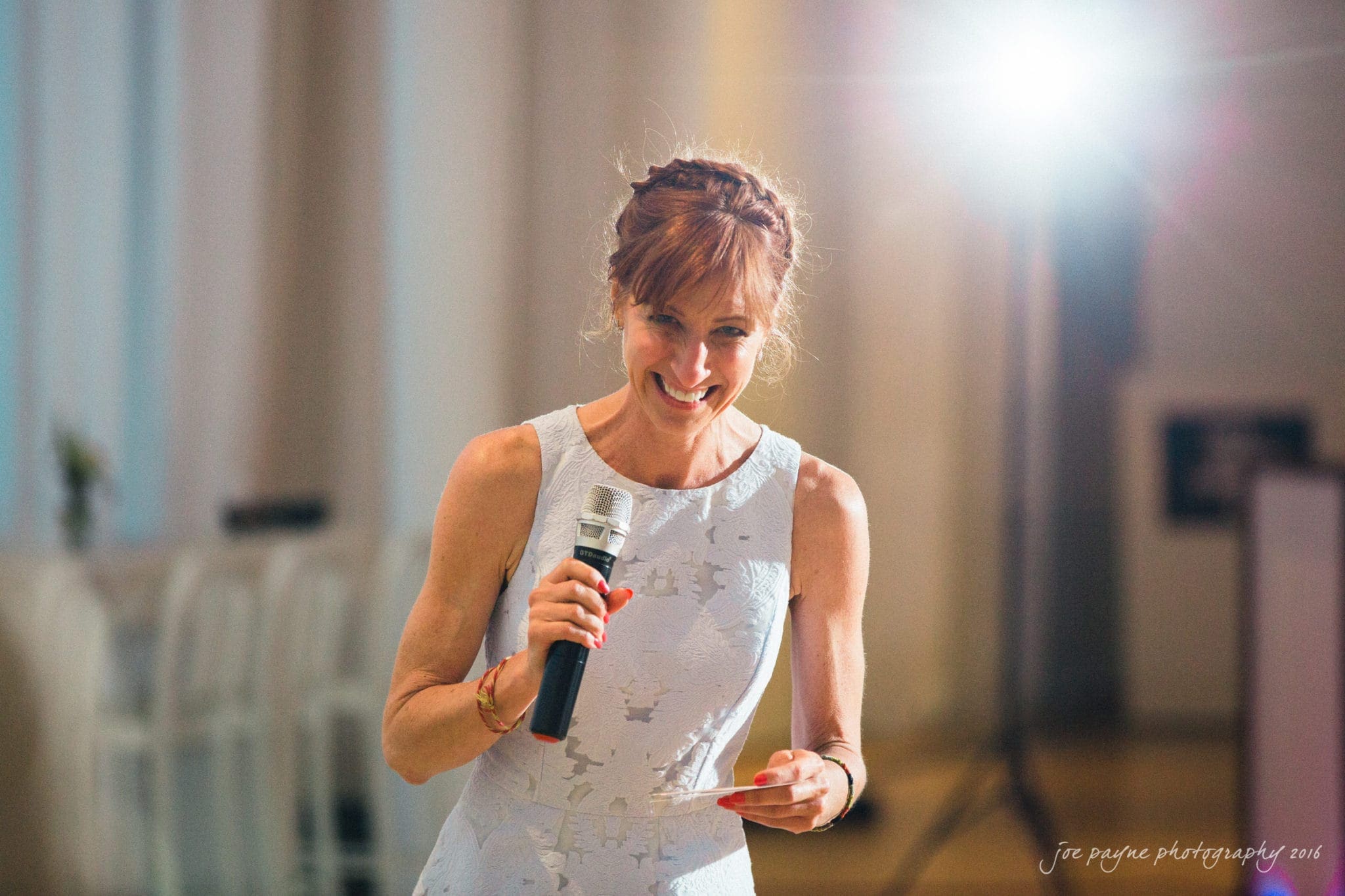 nc museum of art wedding photography - jade & frank A woman in a light blue dress smiles while holding a microphone and a note card. She is standing indoors with bright lighting in the background.