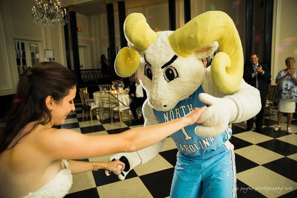 duke chapel & carolina inn wedding - sidney & andrew A bride dances with a person in a North Carolina mascot costume in a formal setting with black and white checkered floor. Guests in the background watch and clap.