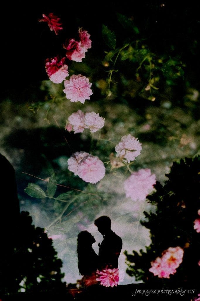 Silhouettes of a couple are surrounded by a dreamy overlay of pink flowers and greenery, creating a romantic and serene atmosphere.