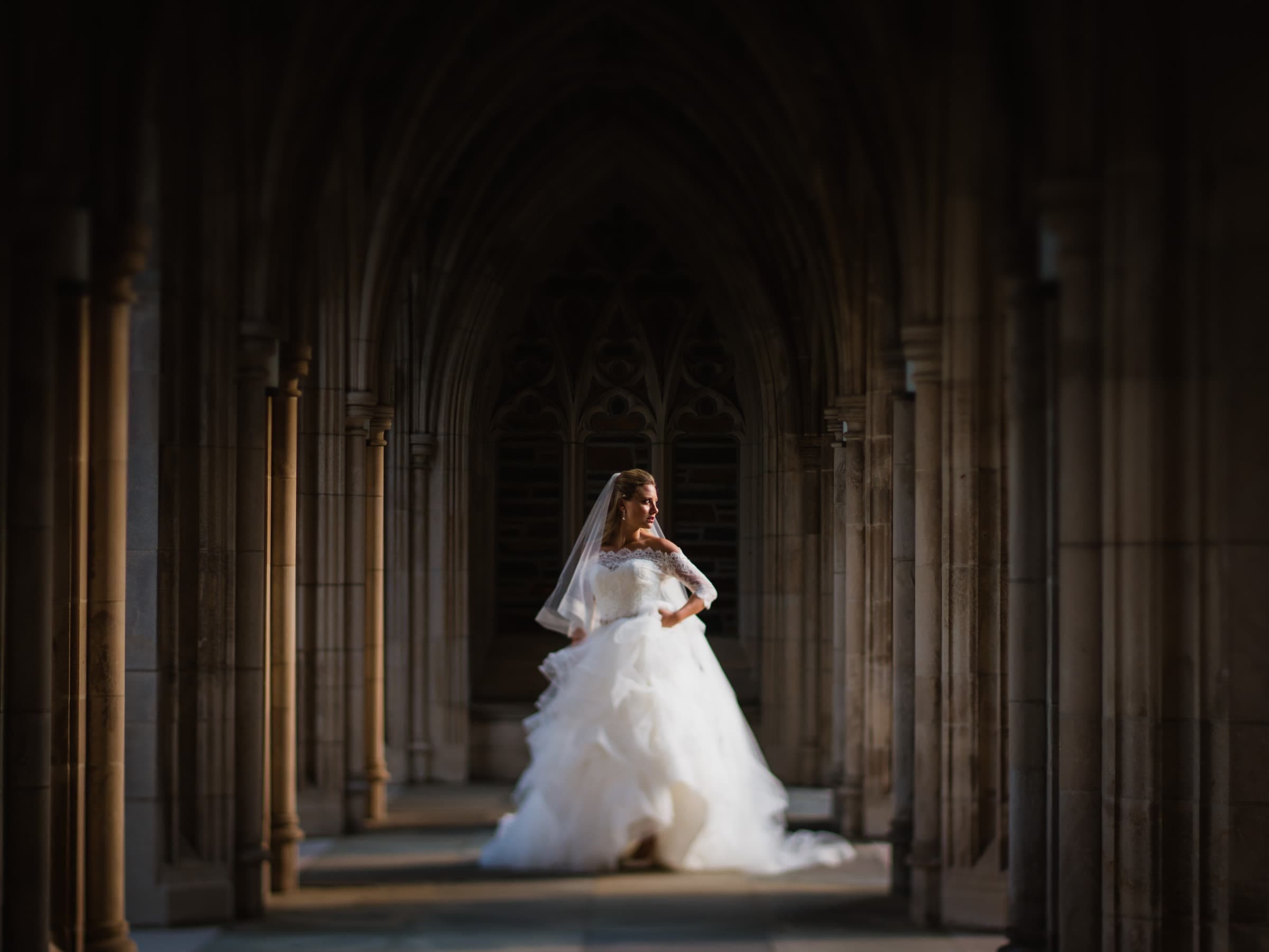 Duke Chapel Weddings A creative fine art bridal portrait of Sara inside the Duke Chapel stone arcades, captured using natural light and a tilt-shift lens to create a beautiful, soft focus.