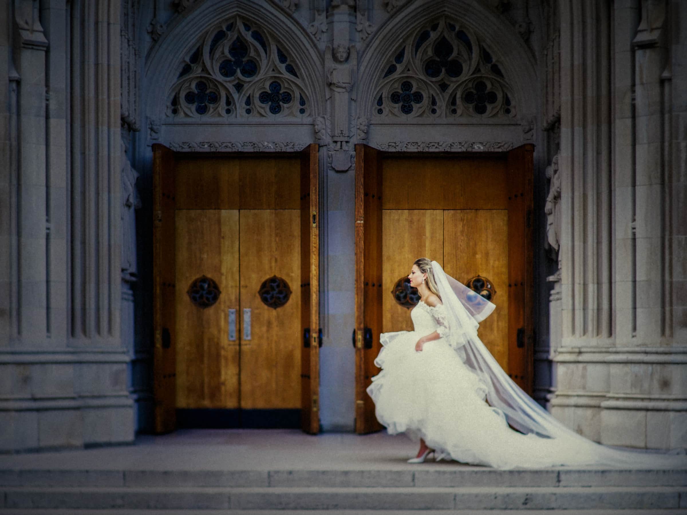 Duke Chapel Weddings A timeless fine art bridal session portrait of Sara capturing the elegant silhouette of her wedding gown against the historic stone walls of Duke University Chapel.