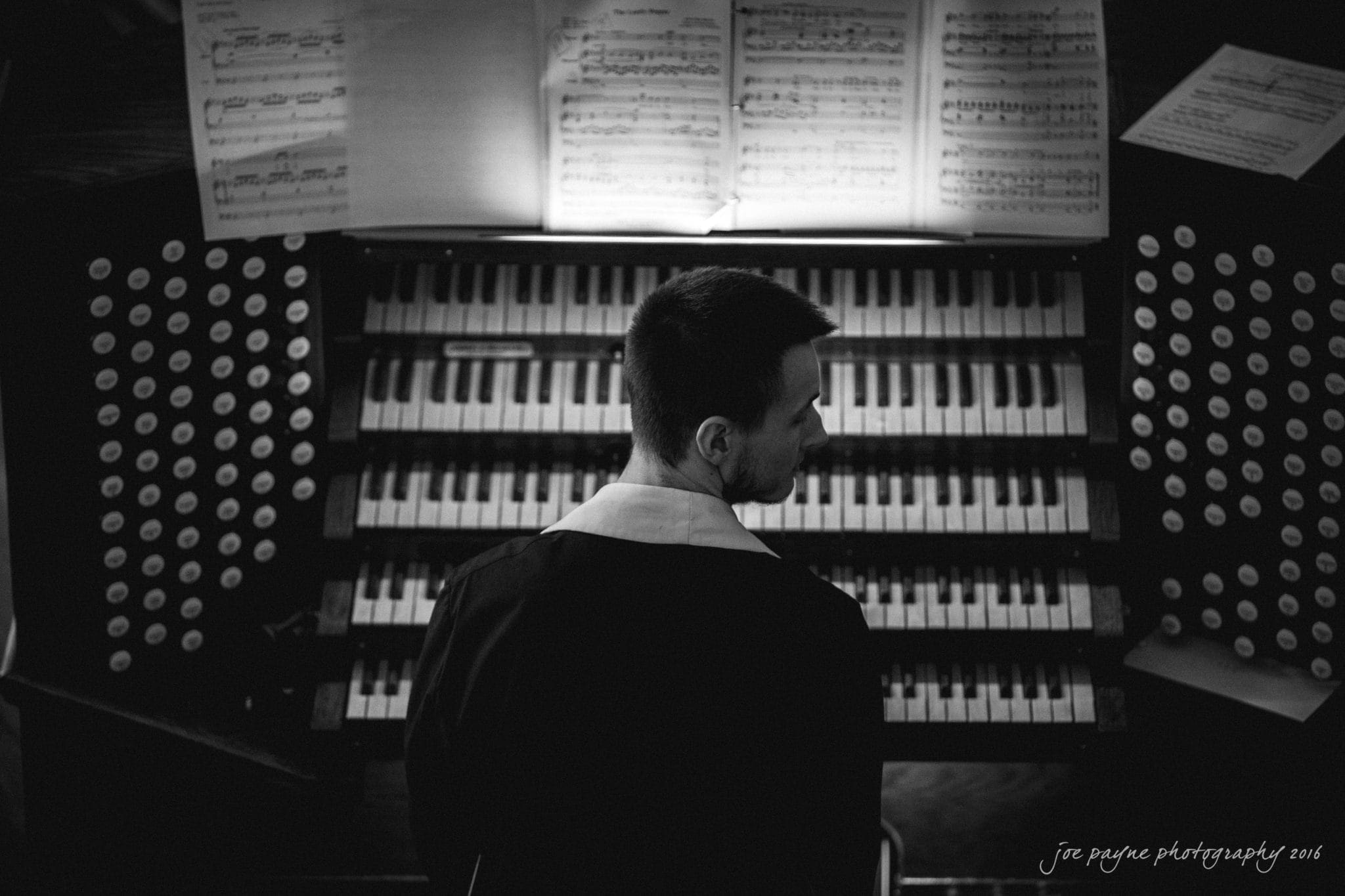 winston-salem nc wedding photography - toni & kevin A person sitting at a large pipe organ, surrounded by rows of keys and stops. Sheet music is open on the stand in front of them. The lighting is dim, creating a contemplative atmosphere.