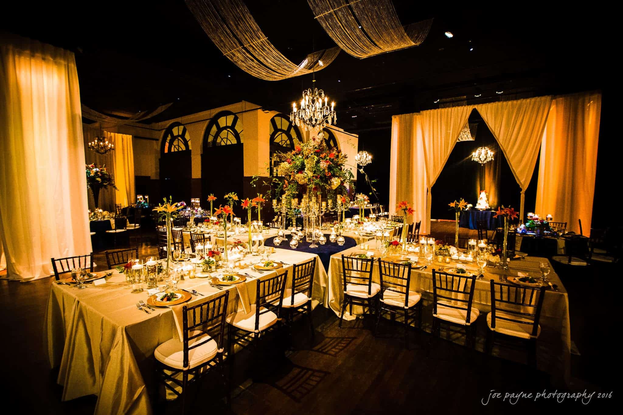 winston-salem nc wedding photography - toni & kevin Elegant wedding reception with beautifully set tables featuring flower centerpieces, candlelight, and draped fabric overhead. Warm, inviting atmosphere with a chandelier and softly lit background.