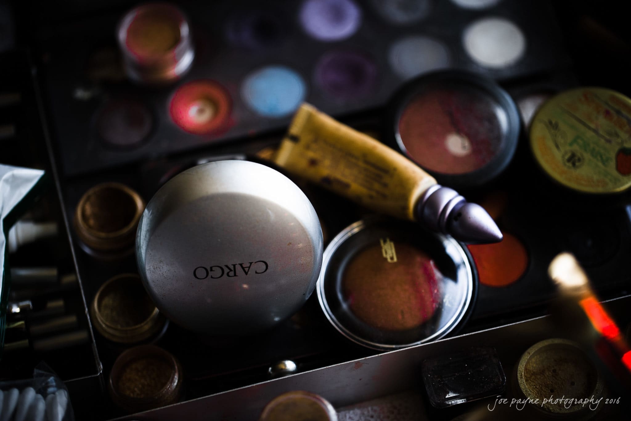 winston-salem nc wedding photography - toni & kevin An assortment of makeup products, including various round compacts, colorful eyeshadow palettes, and a tube of primer lying on a dark surface. The brand Cargo is visible on one compact.