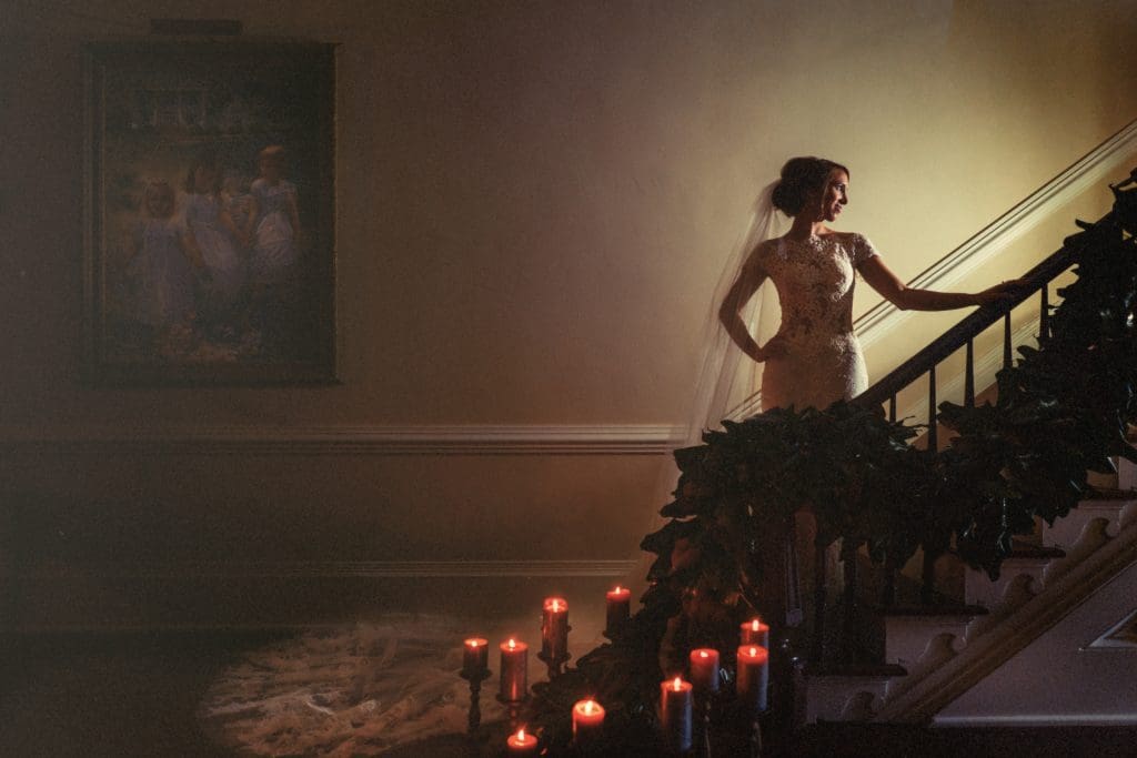 Elegant bridal portrait on the historic staircase at Rose Hill Estate, beautifully framed by candlelight and dramatic low-light mood by Joe Payne.