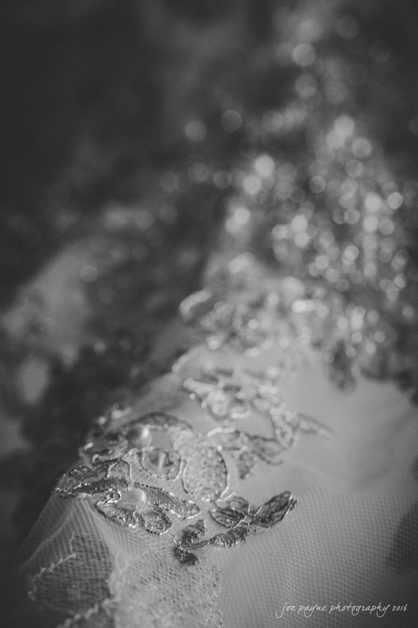 winston-salem nc wedding photography - toni & kevin Close-up of intricate lace embroidery on a fabric, featuring delicate floral patterns. The image is in black and white, highlighting the texture and detail of the lace.