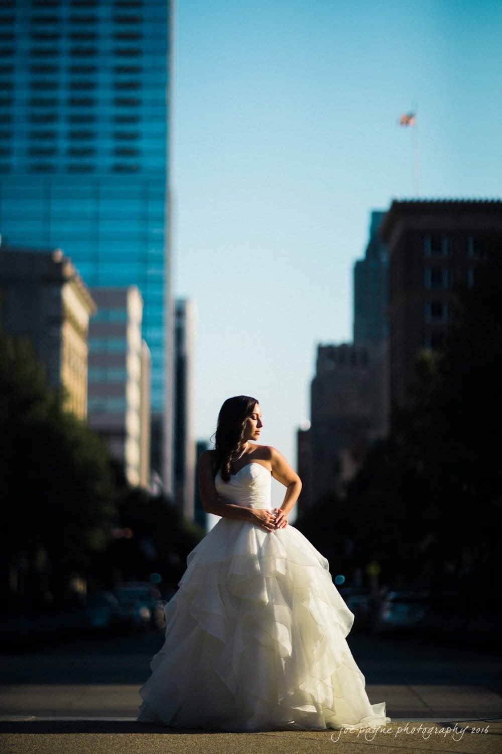 carolina inn wedding photography - kristen & matthew (x2) A bride in a white gown stands confidently in the middle of a city street, surrounded by tall buildings. The sun casts dramatic shadows, highlighting her dress.