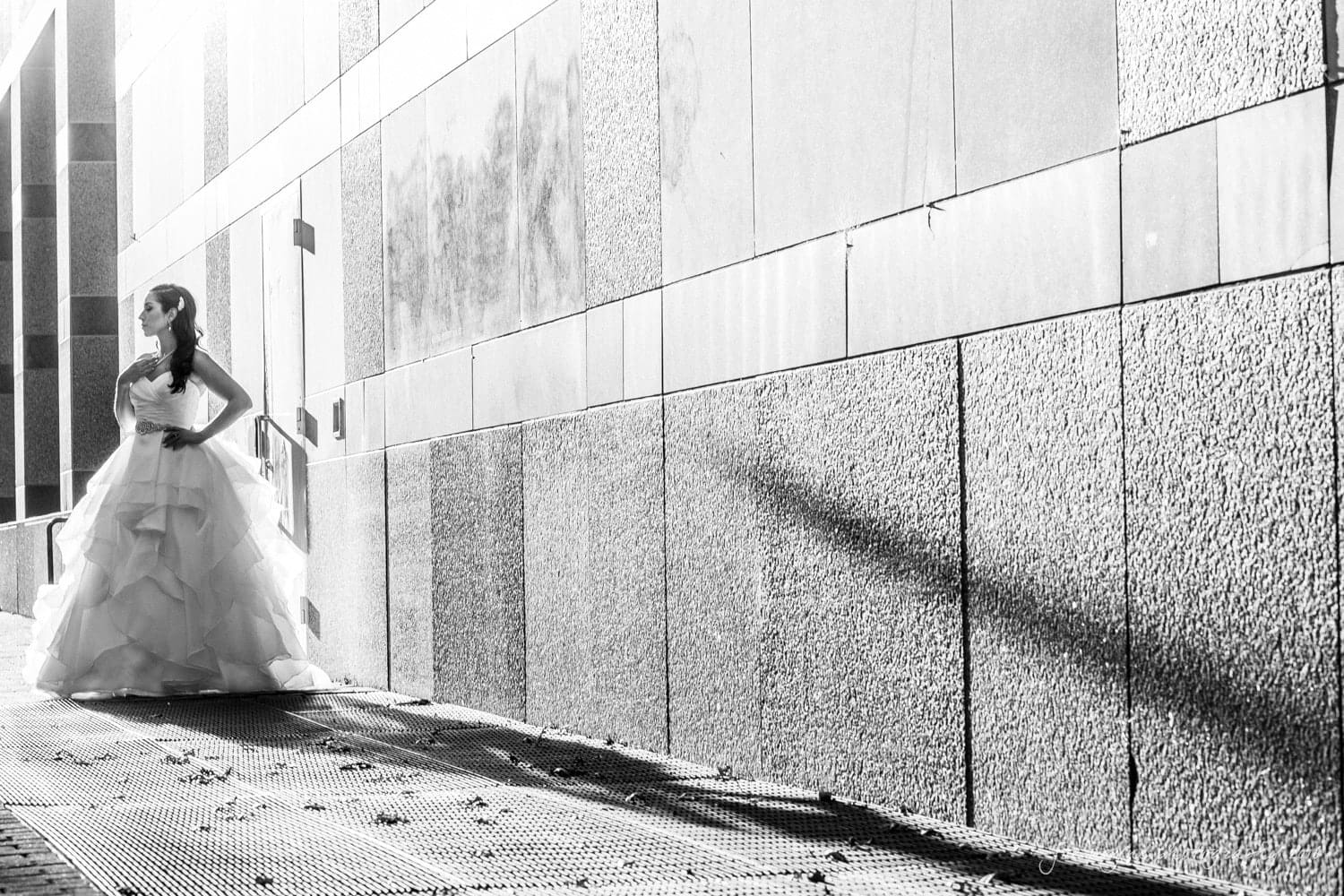 carolina inn wedding photography - kristen & matthew (x2) A woman in a flowing gown stands confidently in a sunlit alley with modern, textured walls. Long shadows stretch across the ground.