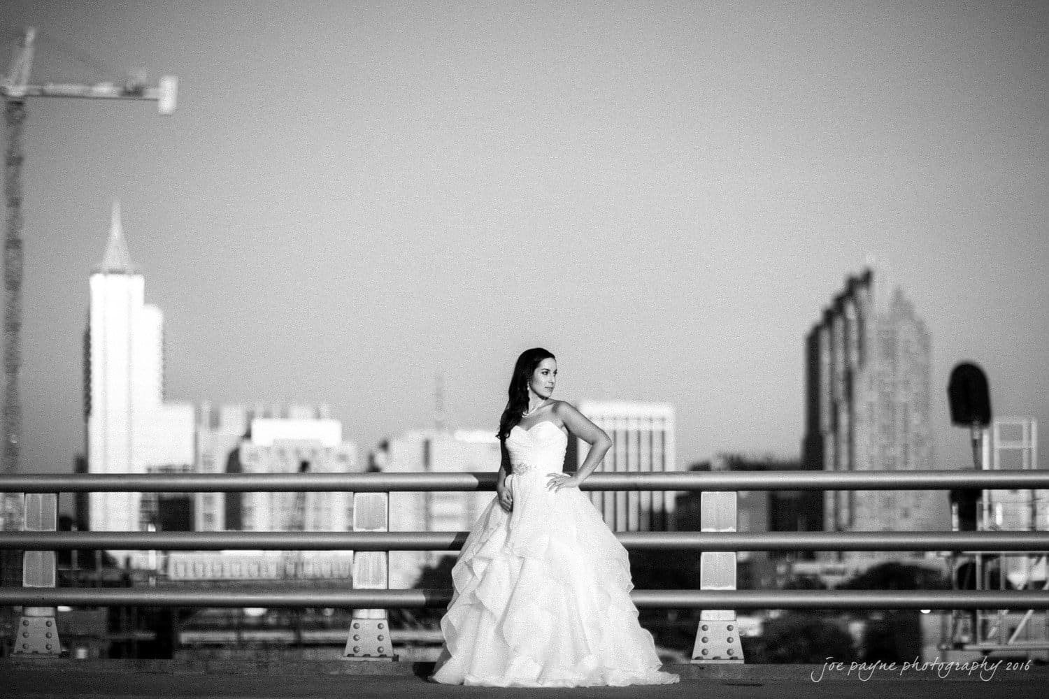 carolina inn wedding photography - kristen & matthew (x2) A bride in a flowing white gown poses confidently on a bridge, with a city skyline in the background. The scene is captured in black and white, highlighting the contrast between the brides dress and the urban setting.