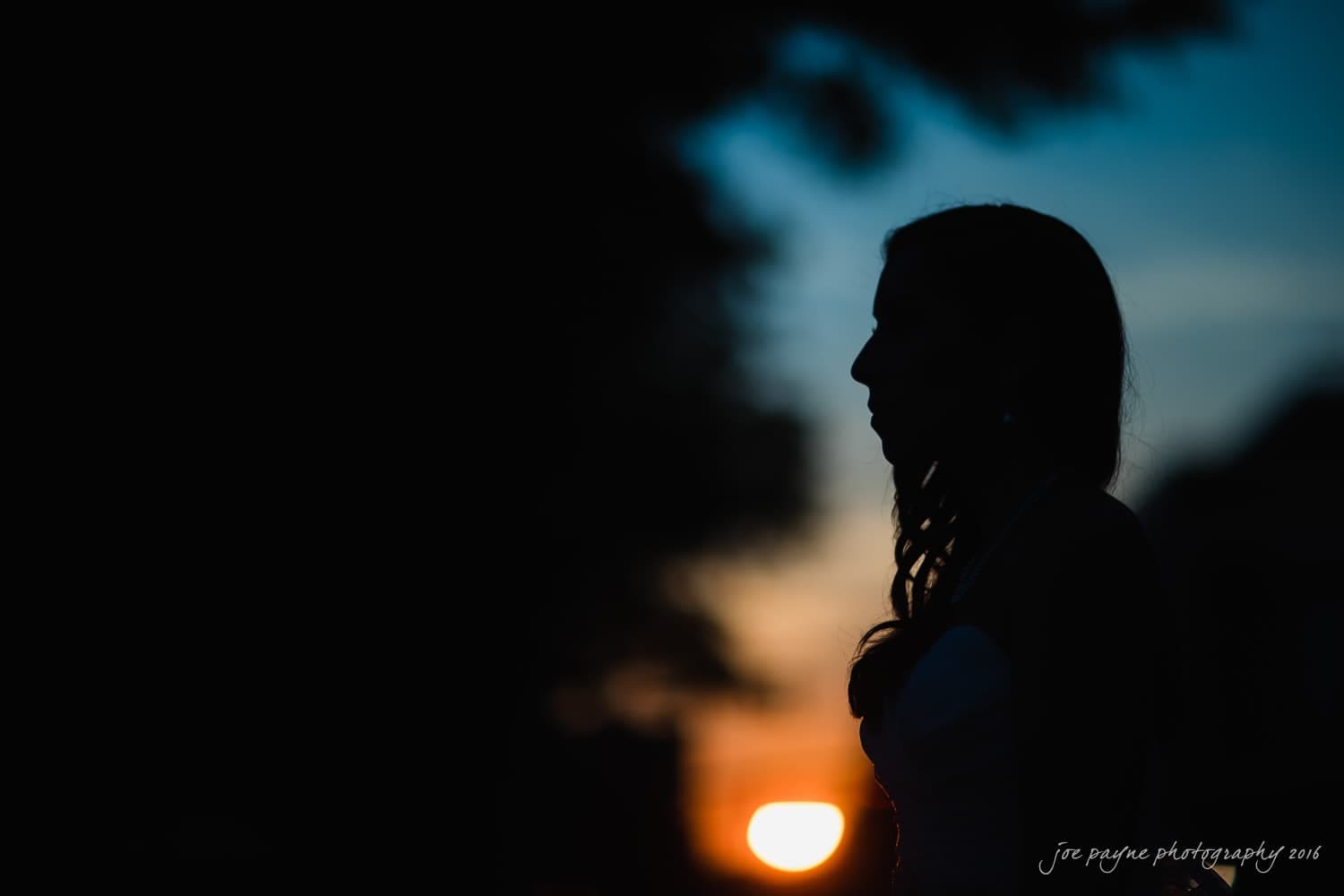 carolina inn wedding photography - kristen & matthew (x2) Silhouette of a person against a sunset backdrop, with the sun low in the sky and the horizon blending into dark trees.
