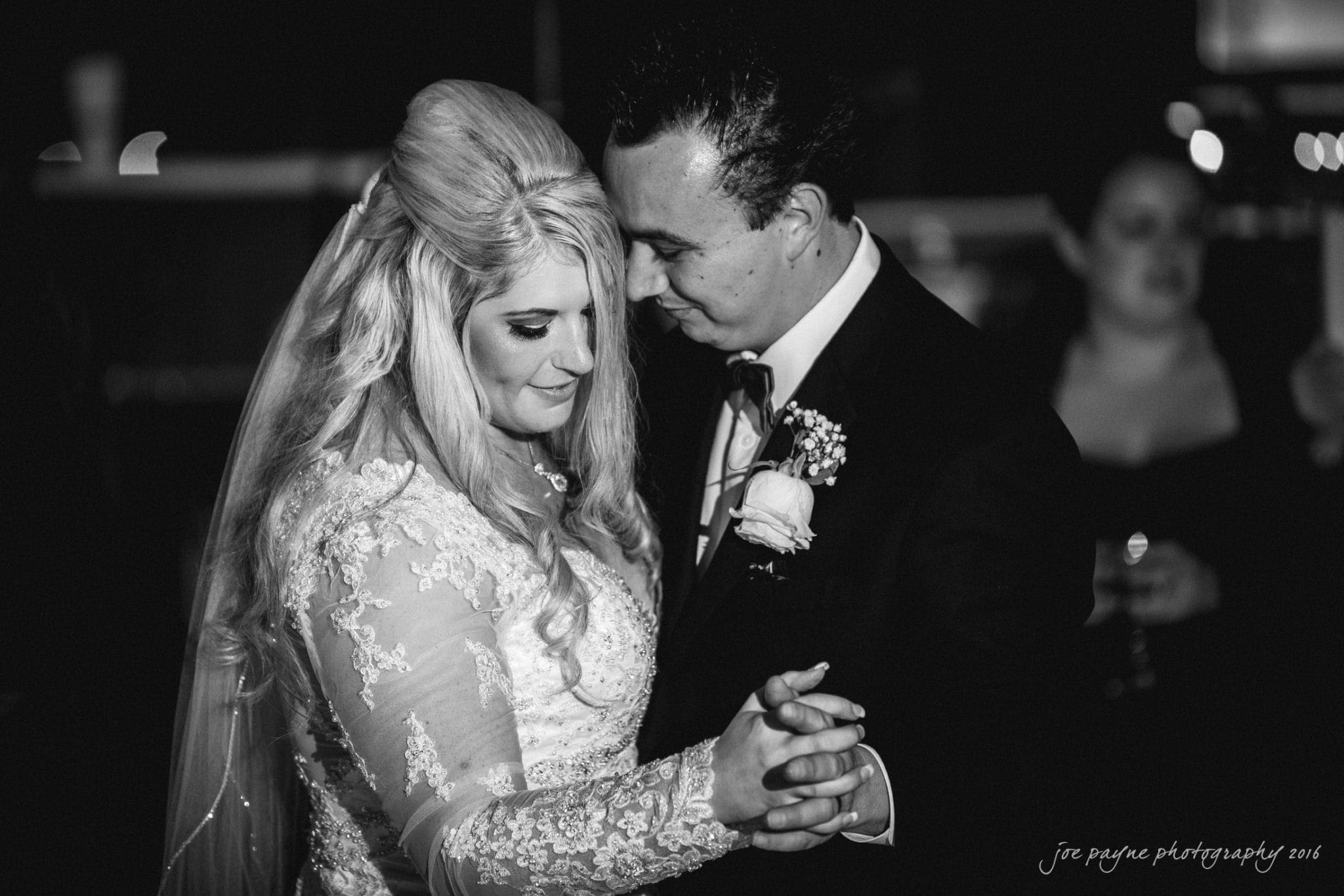 shady wagon farm wedding photography - danielle & josh A bride and groom share a romantic first dance. The bride wears a lace gown and veil, while the groom is in a dark suit with a boutonniere. They are looking at each other lovingly in a softly lit setting.