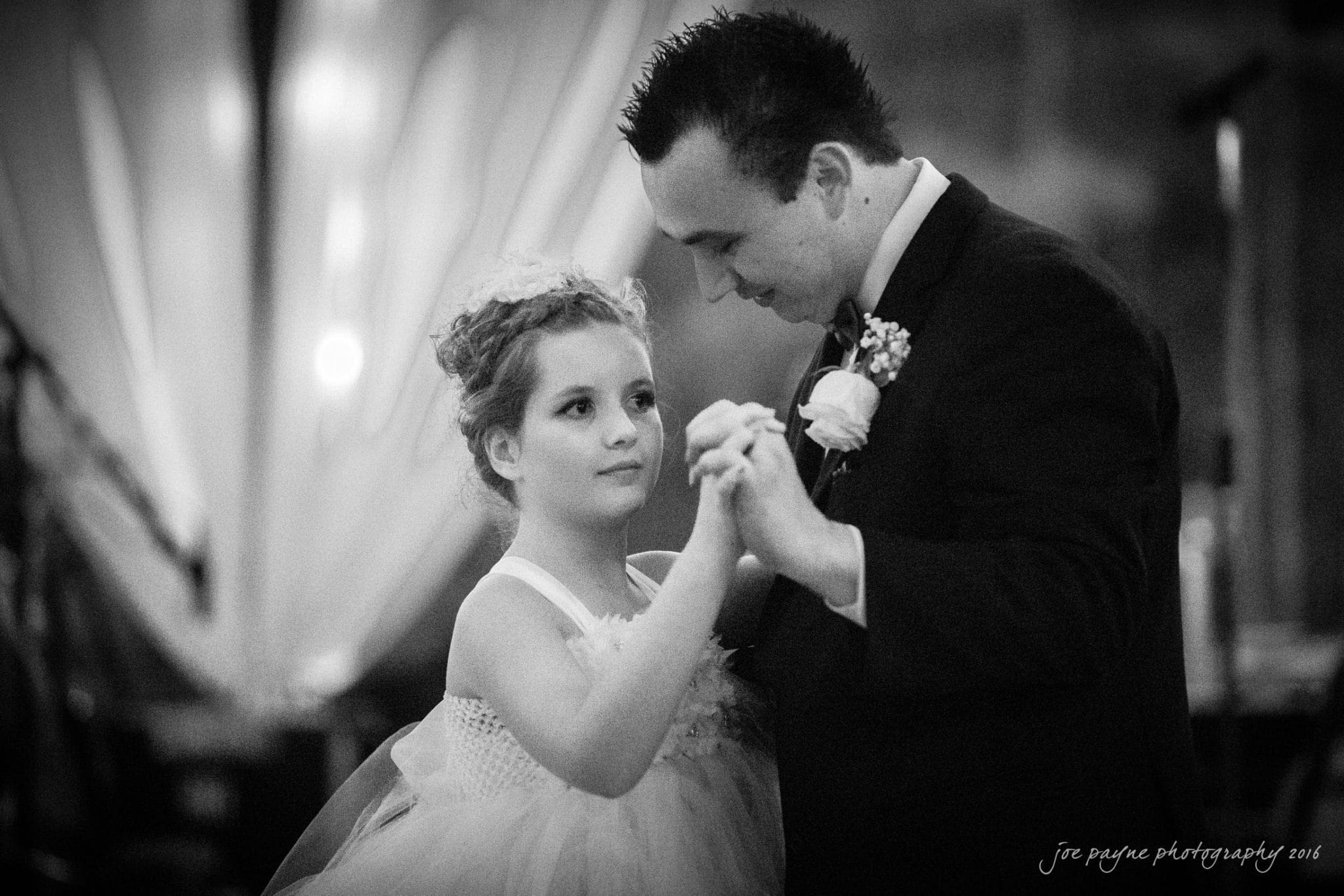 shady wagon farm wedding photography - danielle & josh A man in a suit and a young girl in a white dress share a dance at an event. The background is softly blurred, highlighting their expressions.