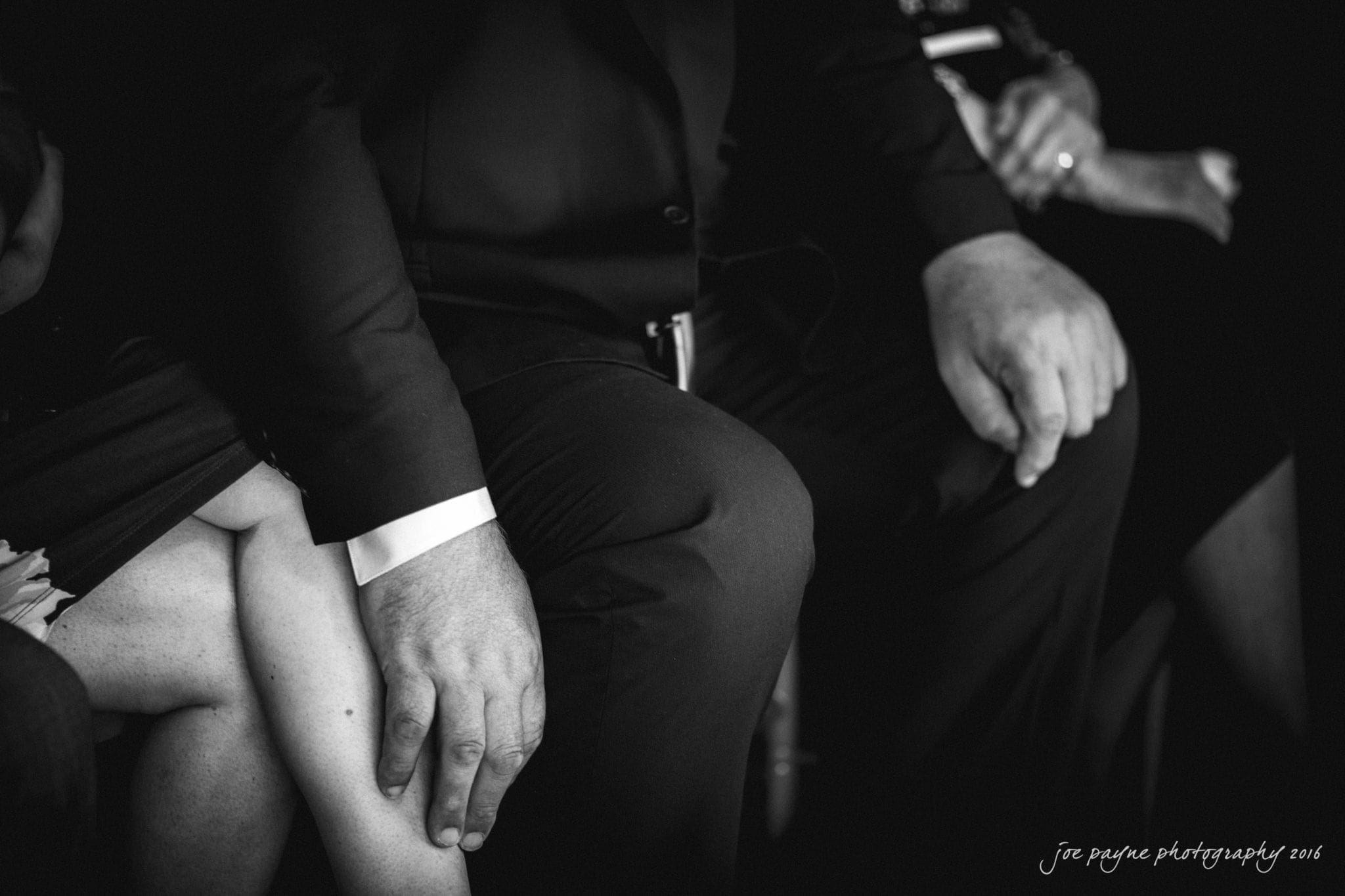 city club wedding photographer - lauren & adam Black and white photo of people seated closely. A mans hand rests on a womans knee, both dressed in formal attire. The image captures a moment of intimacy and connection.