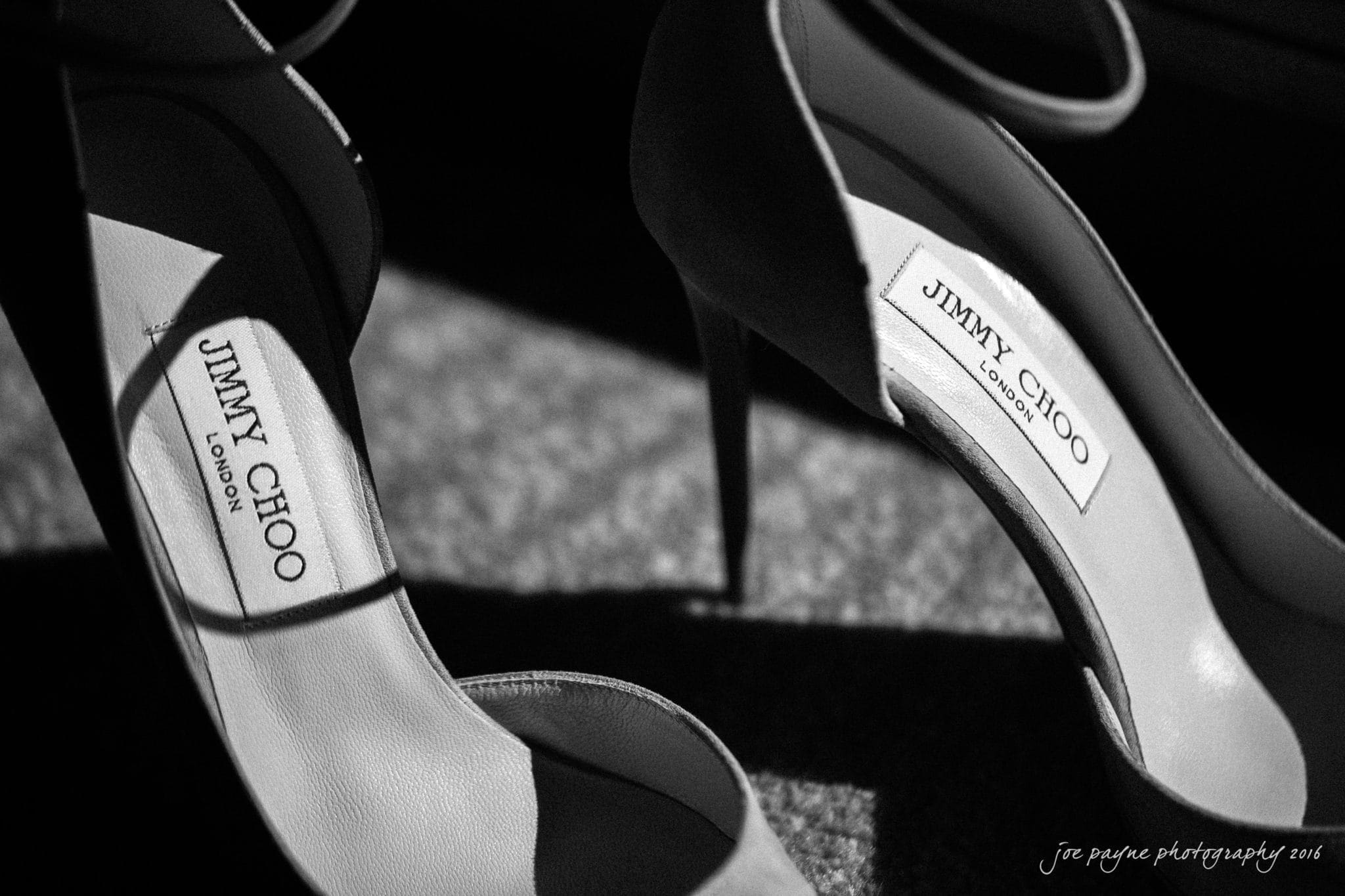 city club wedding photographer - lauren & adam Black and white image of two elegant high-heeled shoes with visible Jimmy Choo London labels on the insoles. The shoes are positioned in soft lighting, creating a sophisticated and stylish atmosphere.