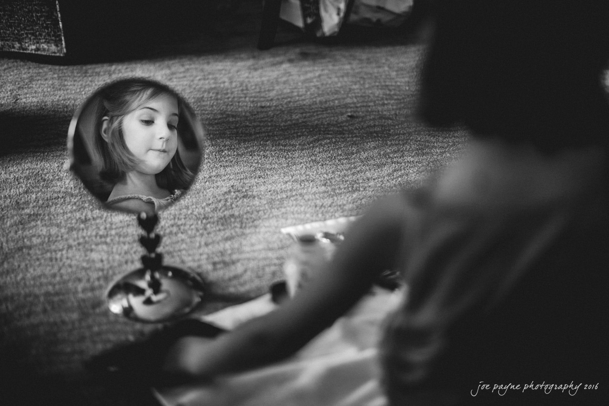 city club wedding photographer - lauren & adam A girl gazes into a round mirror, her reflection clear in the glass. The background and surroundings are blurred, focusing attention on her thoughtful expression. The image is in black and white, creating a nostalgic atmosphere.