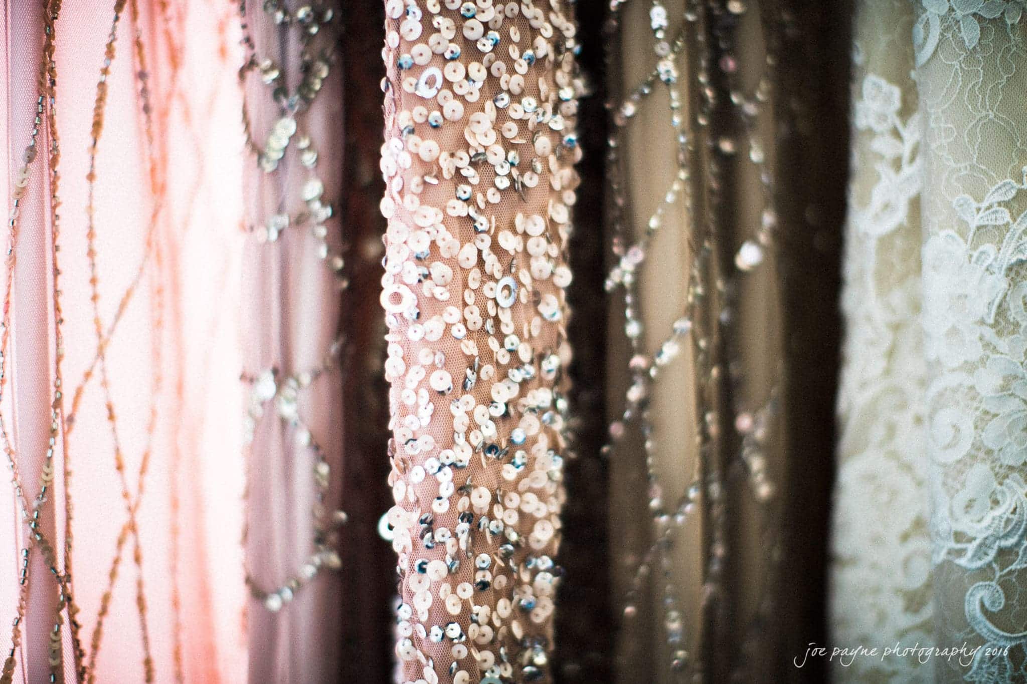 city club wedding photographer - lauren & adam Close-up of various fabric textures and patterns, featuring pink and white lace, shimmering sequins, and beads. The fabrics hang vertically, capturing light and detail in an elegant display.