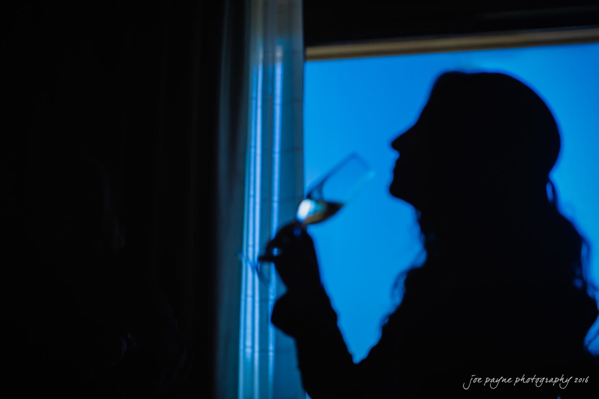 city club wedding photographer - lauren & adam A silhouette of a person holding a wine glass, with light streaming through a window behind them, creating a blue and dark contrast.