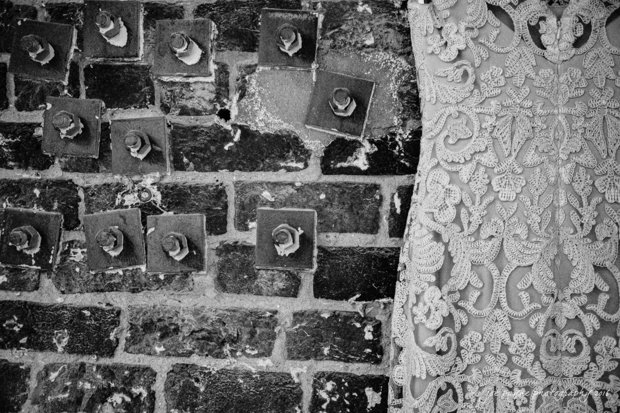 cloth mill at eno river wedding - eleanna & michael Black and white photo of a brick wall with protruding bolts on one side and a close-up view of an intricately embroidered lace fabric on the other side.