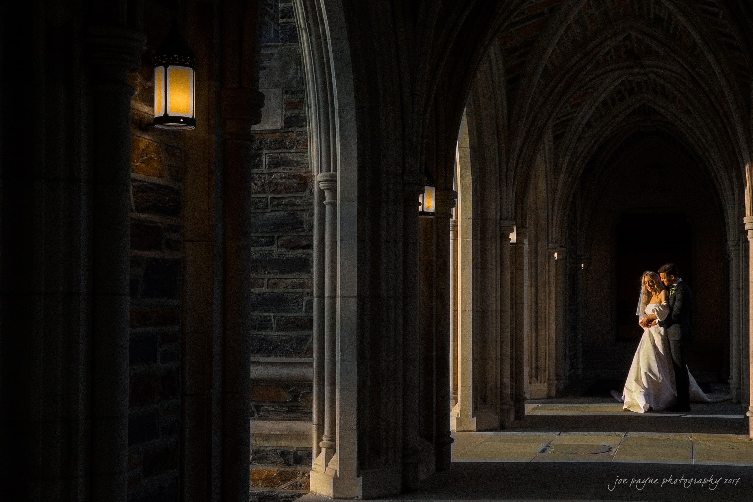 Duke Chapel Weddings A golden hour wedding portrait in the Duke Chapel arcades, featuring the couple elegantly posed and beautifully lit by the warm, direct glow of the setting sun.
