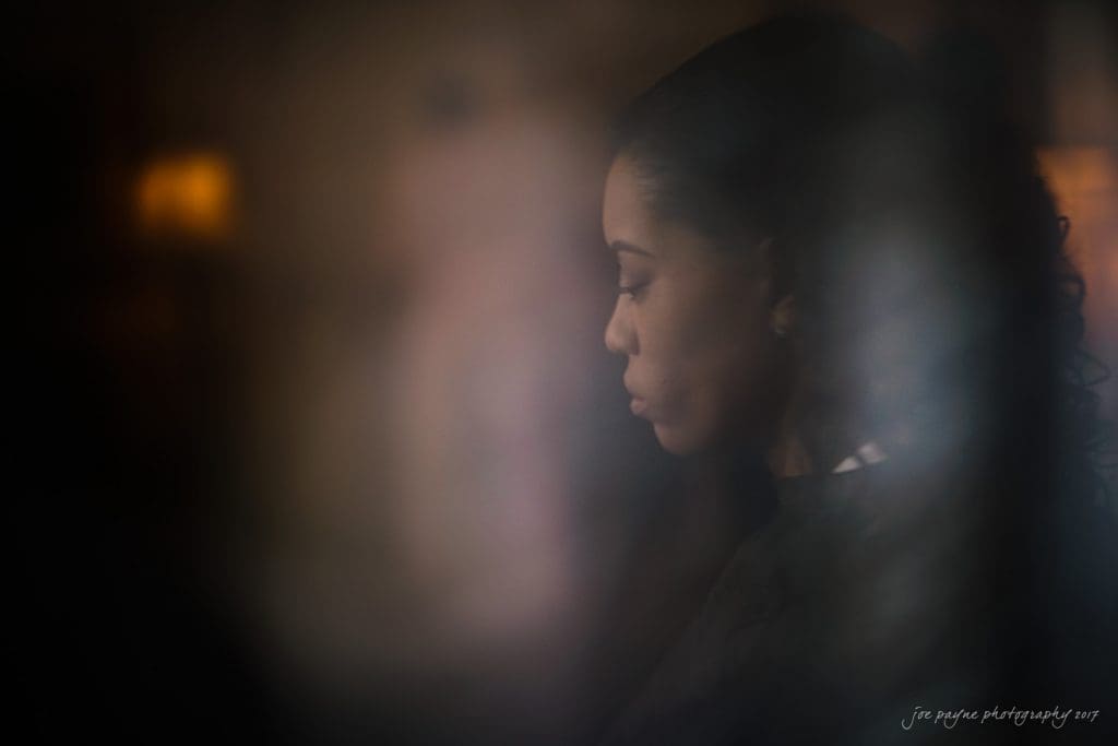 duke gardens wedding photography - jordan & zeke A contemplative woman with long, dark, wavy hair is seen in profile. The image has a soft focus and dim lighting, creating a serene and introspective atmosphere.