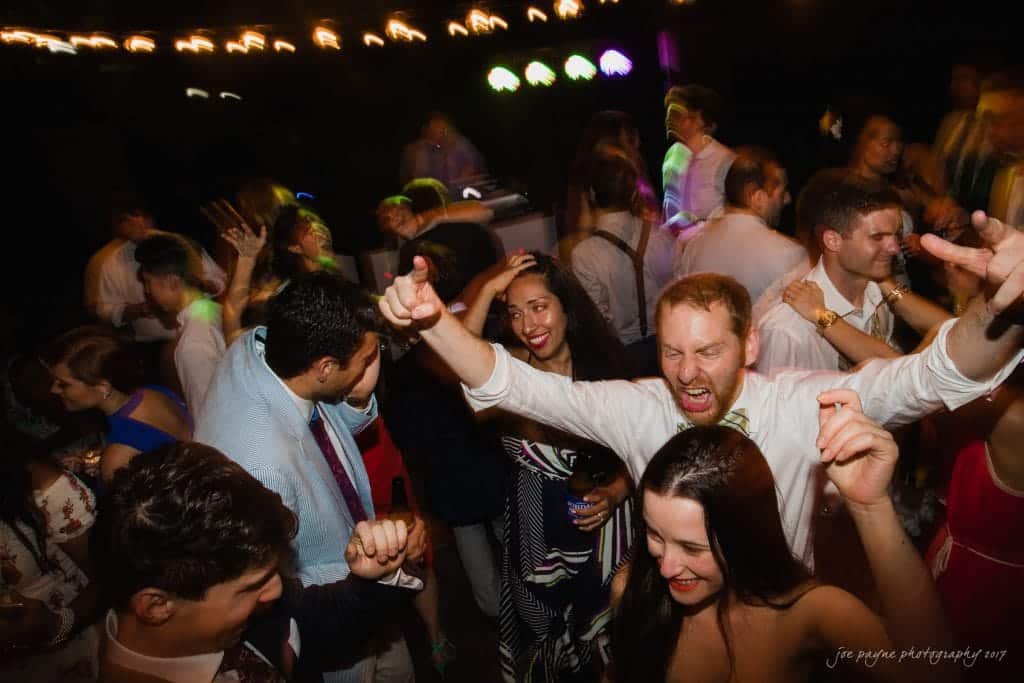 duke gardens wedding photography - jordan & zeke A lively dance floor scene with people enthusiastically dancing under colorful lights. The crowd is diverse, with a mix of men and women in formal attire, showcasing their excitement and energy in a festive atmosphere.