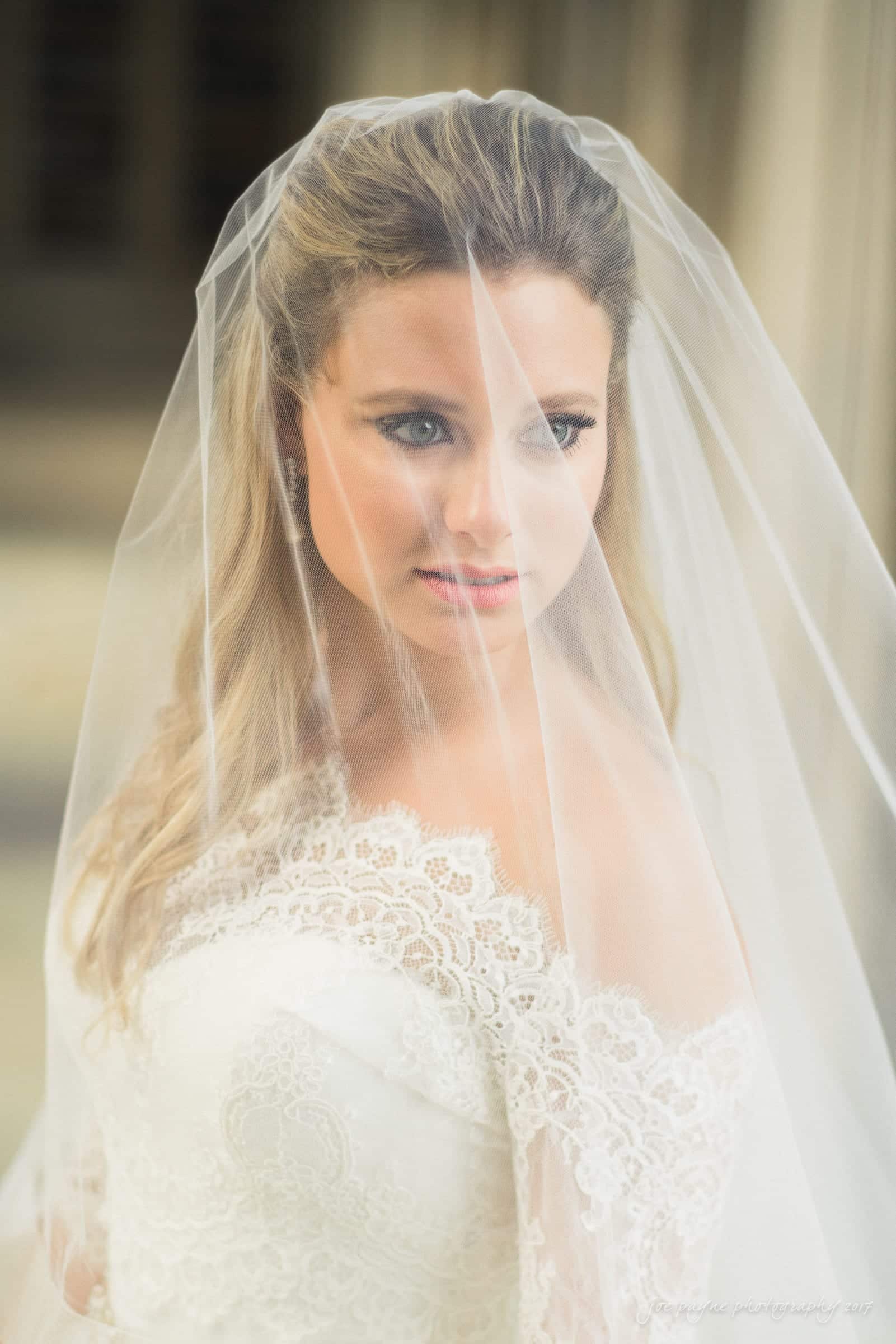 duke chapel wedding photography - sara's bridal session A bride wearing a lace wedding gown and veil gazes softly in the ambient light. The focus is on her serene expression and intricate lace details.
