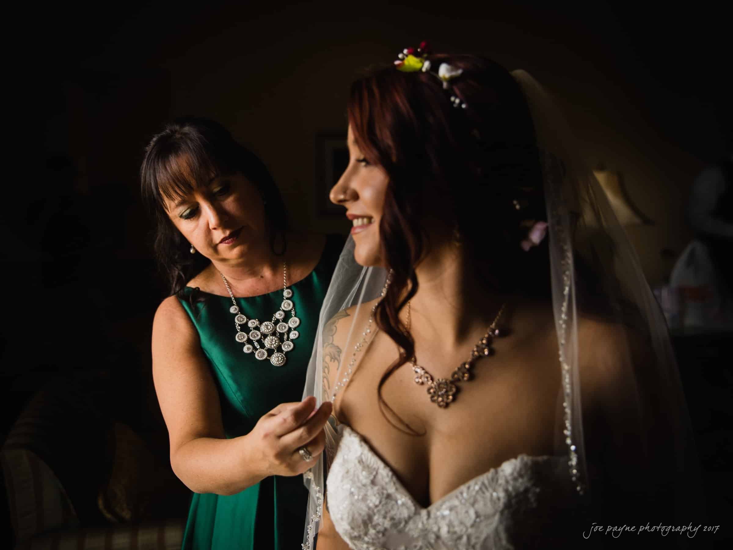 river landing country club wedding - megan & chad A bride in a white dress and veil smiles as a woman in a green dress adjusts her veil. They are indoors, with soft lighting.
