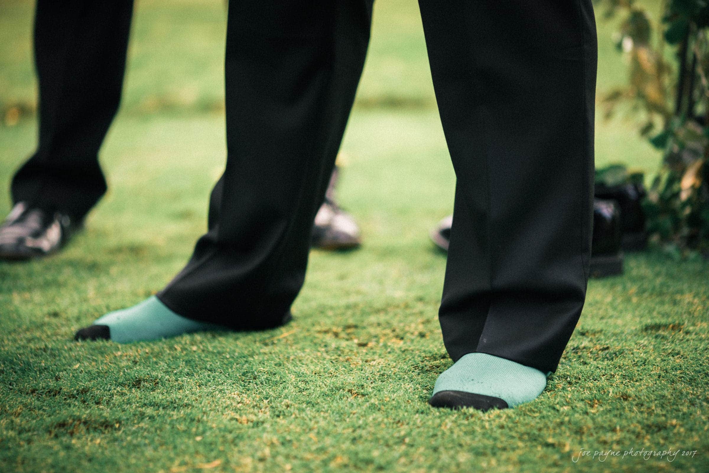 river landing country club wedding - megan & chad A person wearing black pants stands on grass in green socks, with black shoes visible nearby.