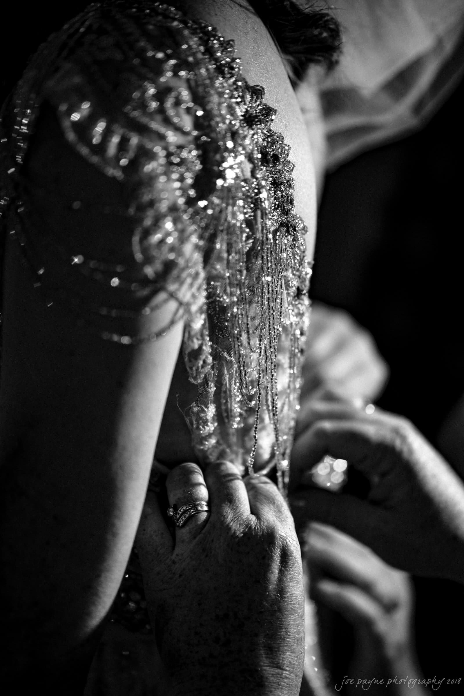 A close-up black and white image of a person adjusting an ornate dress adorned with sequins and beads. The focus is on hands delicately working with the intricate details of the fabric.