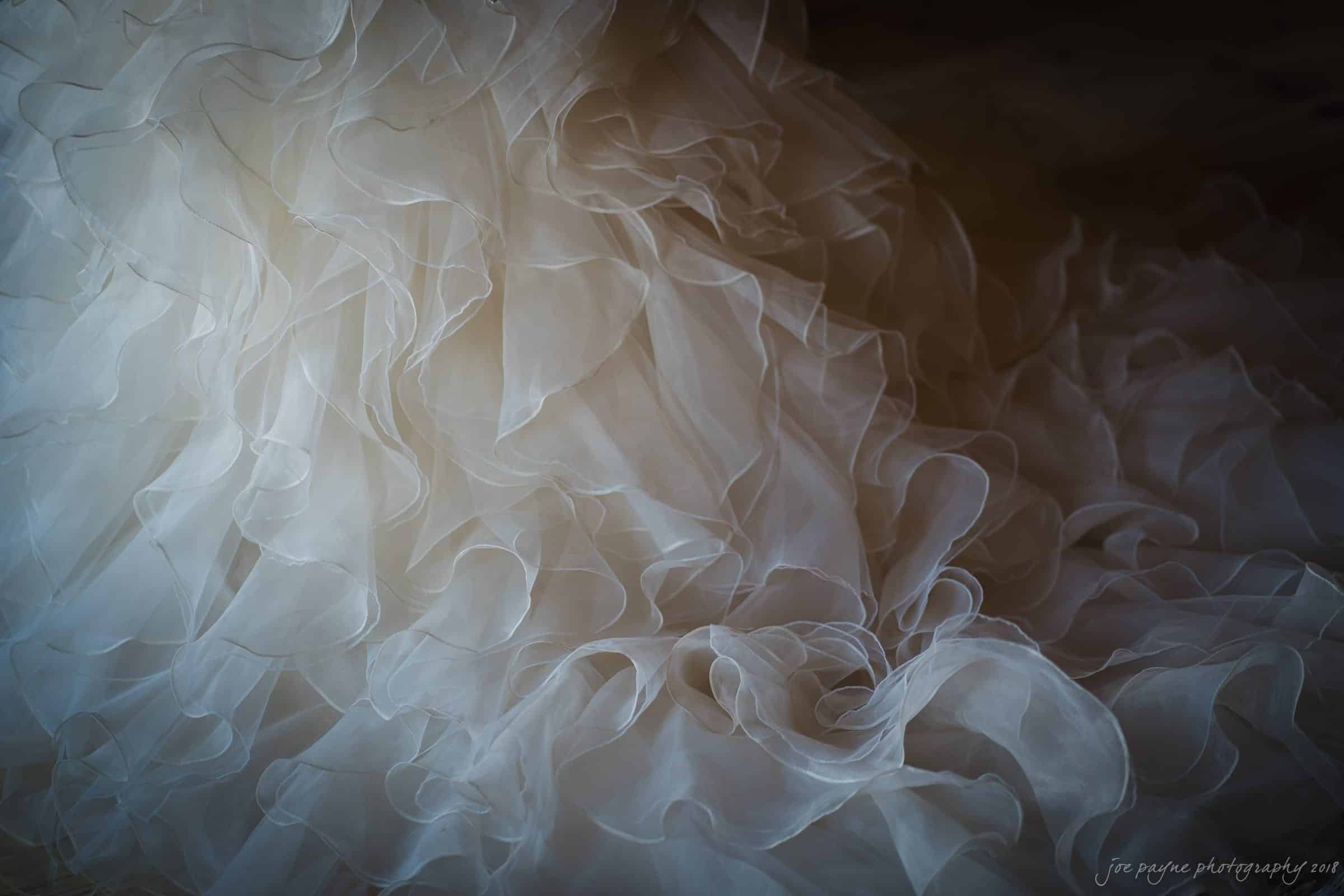 pavilion at carriage farm wedding - ashley & devon Close-up of delicate, layered ruffles of a white or ivory wedding gown fabric, creating a soft and ethereal texture. Bright lighting highlights the intricate translucent material.