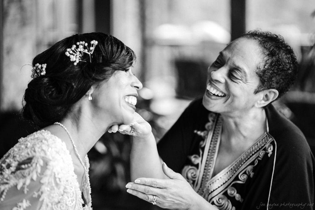 biltmore wedding photographer - anneké & andrew A bride in an ornate dress and floral hairpiece smiles lovingly at an older woman with short hair, who gently touches the brides chin. Both women are laughing and looking at each other in a moment of joy.