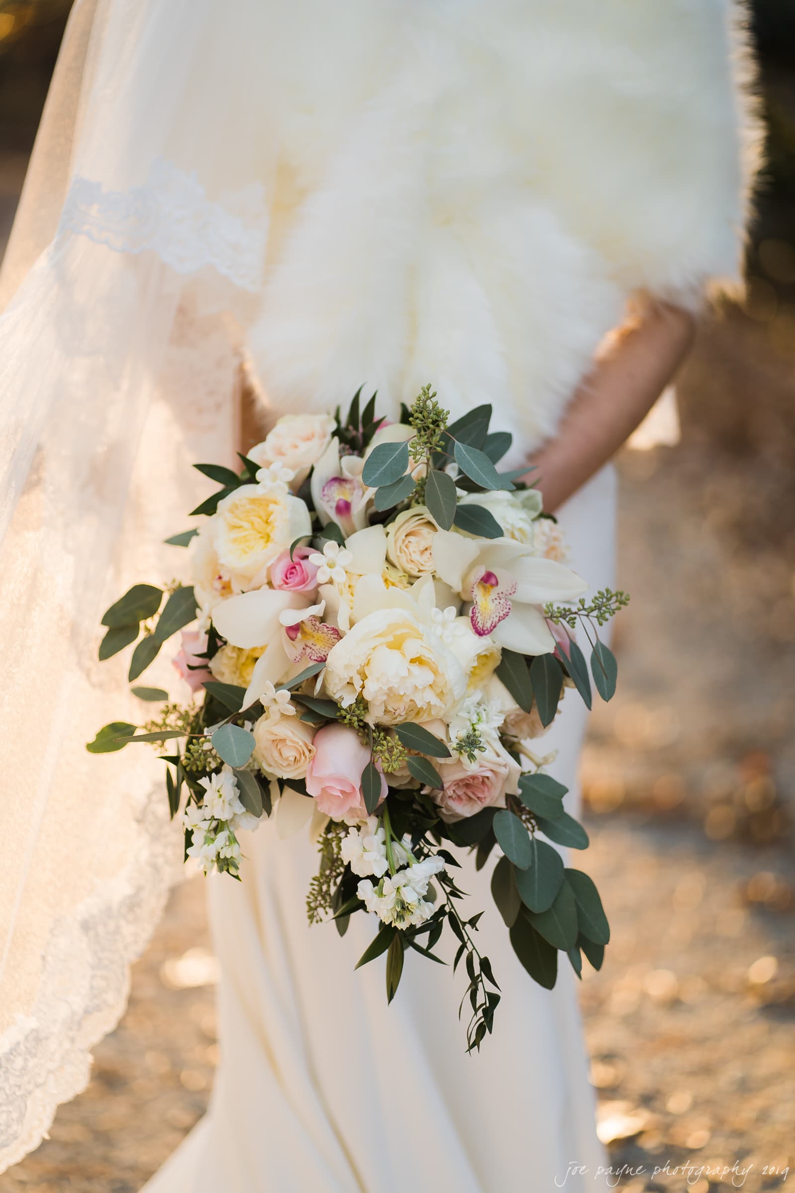carolina inn & duke chapel wedding - kathleen & michael A bride holds a bouquet of white and pink flowers, including roses and orchids, with greenery. She is wearing a white dress with a veil, standing outdoors with soft, warm lighting.