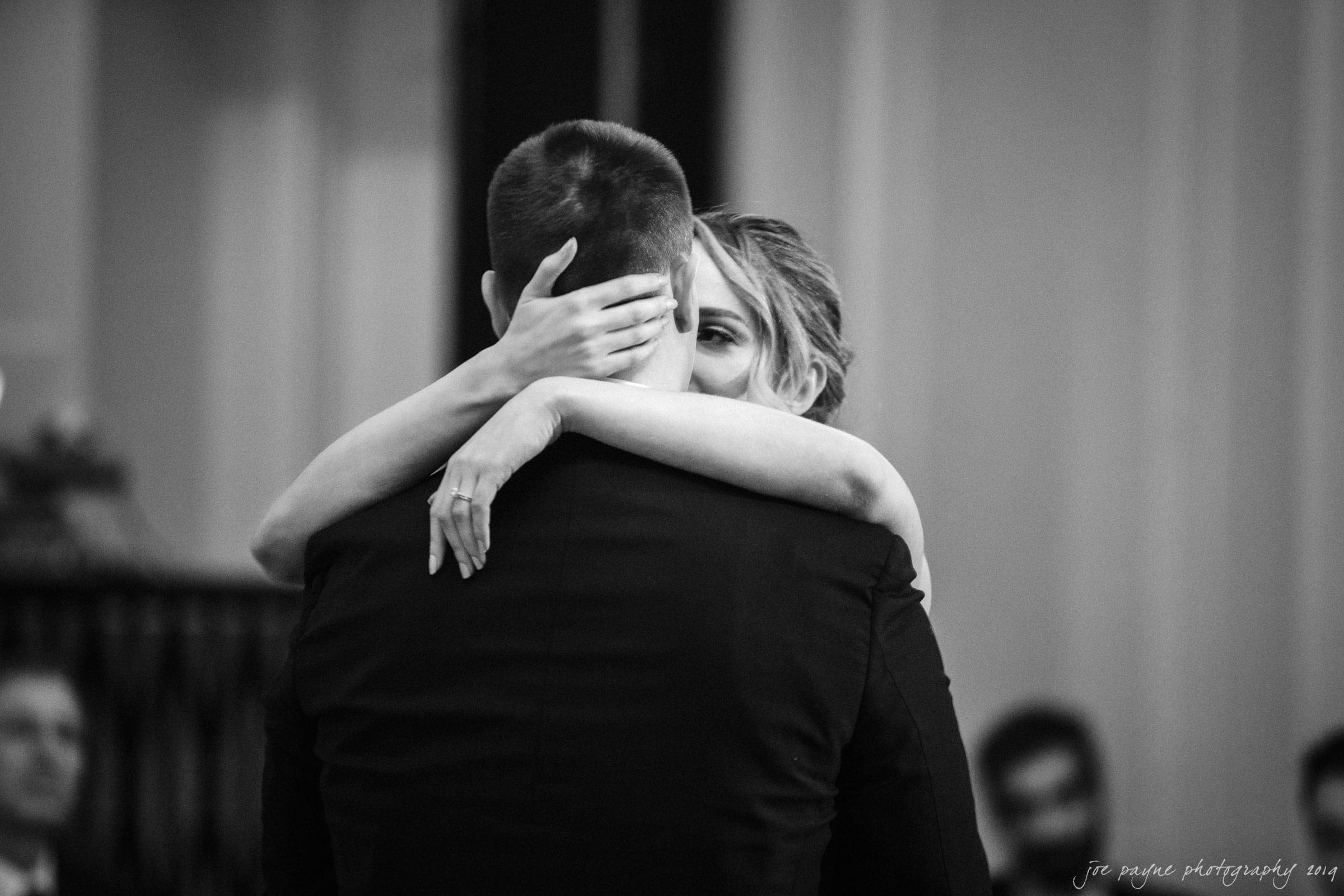 carolina inn & duke chapel wedding - kathleen & michael A couple embraces closely during a dance, with the womans arms wrapped around the mans neck. They are in a softly lit room, creating an intimate and romantic atmosphere. The image is in black and white.