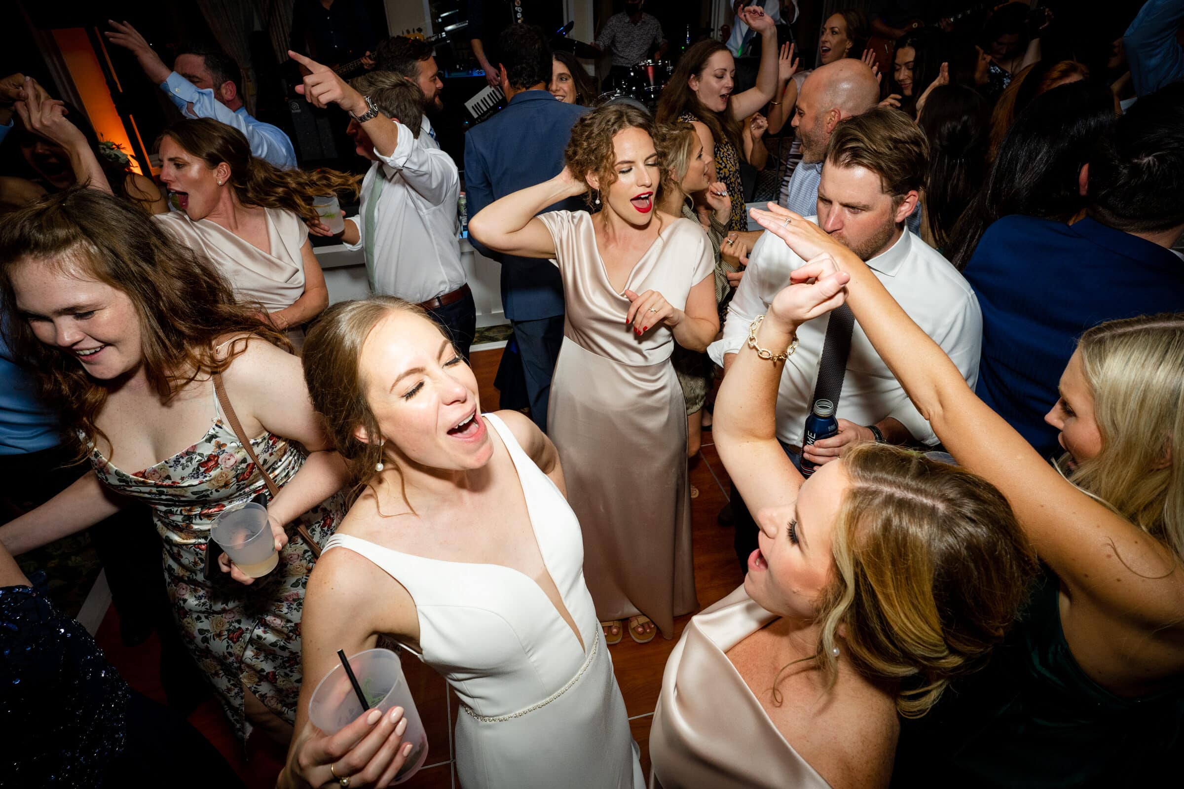 pinehurst wedding photography - lindsey & brendan A lively dance floor scene at a party, with people in formal attire. They are joyfully dancing and socializing, with some holding drinks. The atmosphere is upbeat and festive, highlighted by vibrant expressions and dynamic poses.